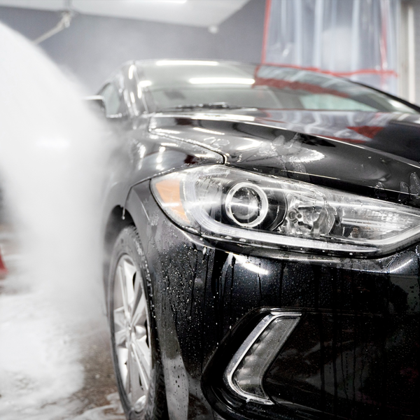 Black car undergoing a thorough hand wash with pH-balanced soap, showcasing water droplets and foam, highlighting Apollo Auto Spa's mobile detailing services.