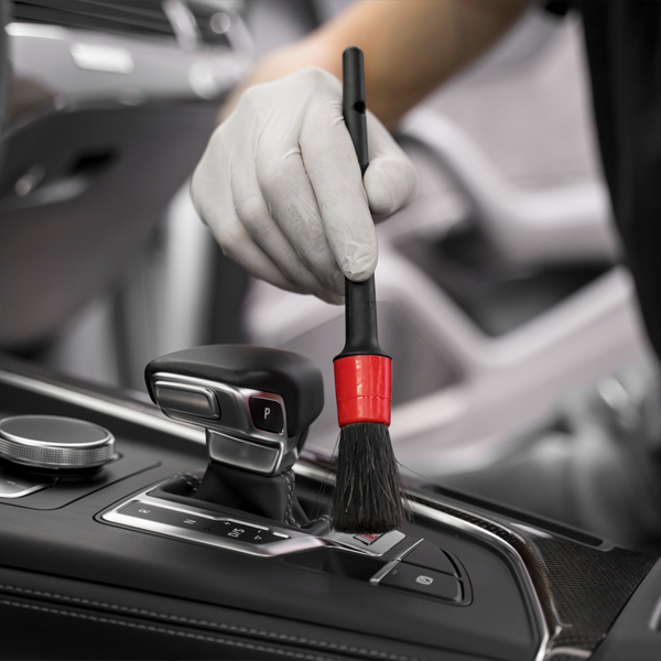 Hand cleaning vehicle interior controls with a detailing brush, showcasing Apollo Auto Spa's professional interior deep cleaning services.