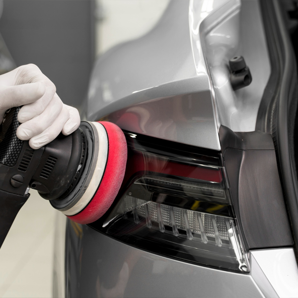 Hand polishing a car's rear tail light using a dual-action polisher, enhancing clarity and shine for improved visibility and aesthetics.